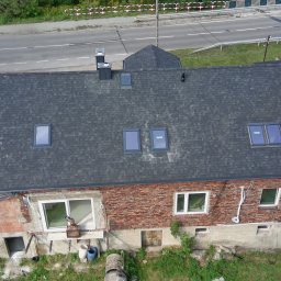 Piotr-bud - Widok z góry na budynek z nowym, ciemnoszarym dachem bitumicznym z oknami dachowymi. Część budynku z cegły, obok zaparkowany biały samochód dostawczy z narzędziami.