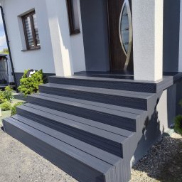 Wojciech Staszel Góral-Drew - Nowoczesne, grafitowe schody wejściowe z desek kompozytowych prowadzące do drzwi domu. Widoczne detale wykończenia i otoczenie budynku.