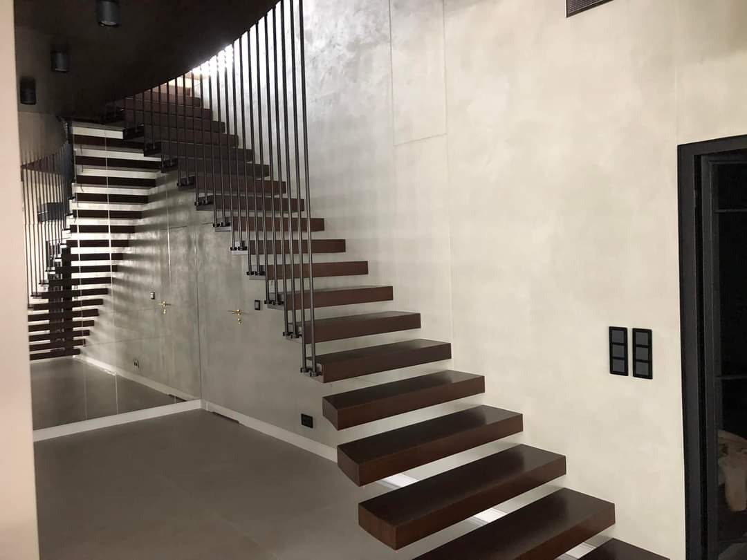 Nowoczesne schody z drewnianymi stopniami i metalową balustradą w minimalistycznym wnętrzu z gładzią na ścianie i lustrzaną ścianą.
