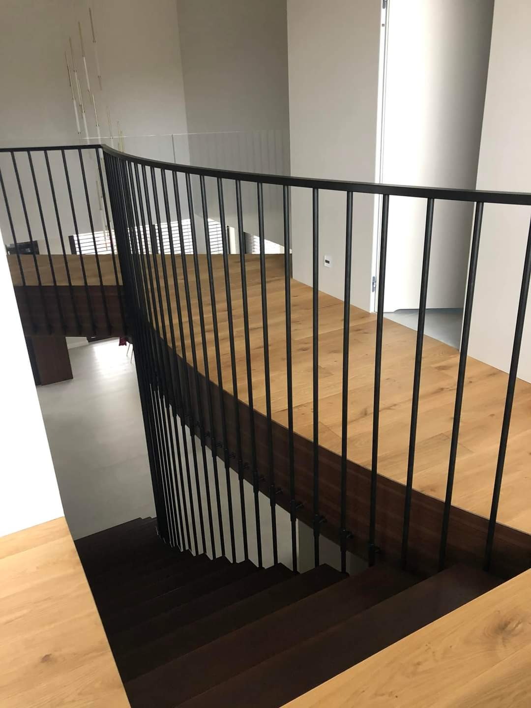 Nowoczesne schody z drewnianymi stopniami i czarną, metalową balustradą, widziane z góry, z elementami minimalistycznego wnętrza w tle.