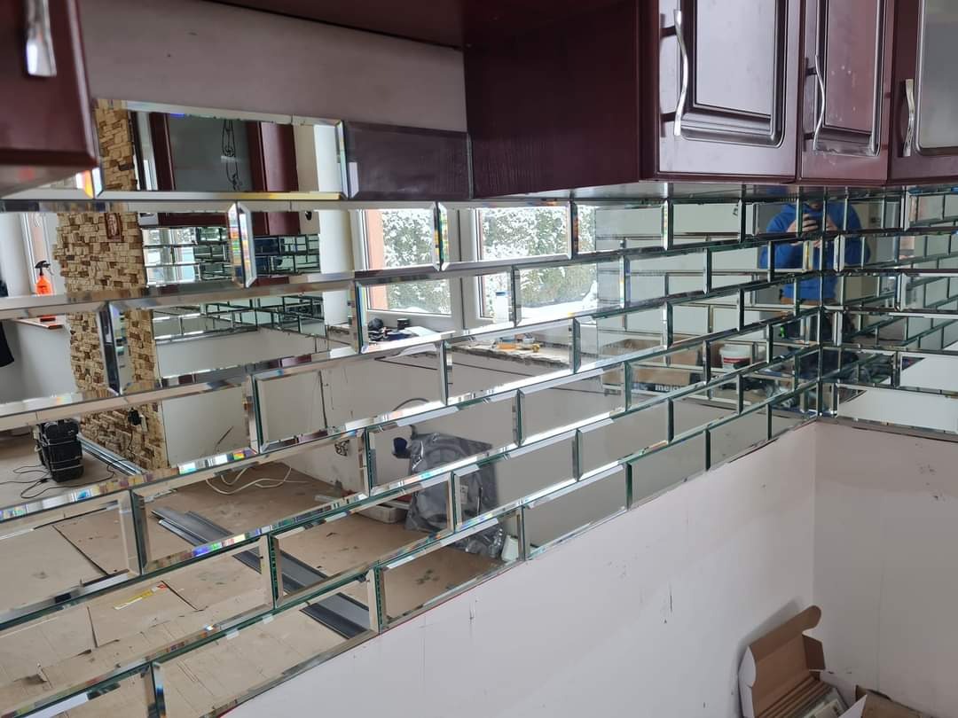 Montaż lustrzanych płytek w kuchni, ułożonych w cegiełkowy wzór, widoczne narzędzia i przygotowane podłoże