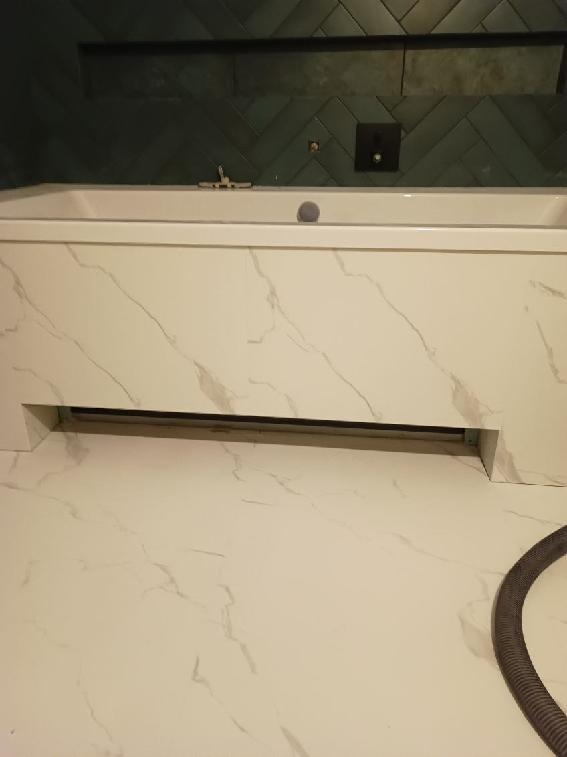 Nowoczesna łazienka z wanną obudowaną płytami imitującymi marmur i zielonymi płytkami ułożonymi w jodełkę na ścianie. Widoczny fragment podłogi wyłożonej płytkami w podobnym stylu do obudowy wanny...