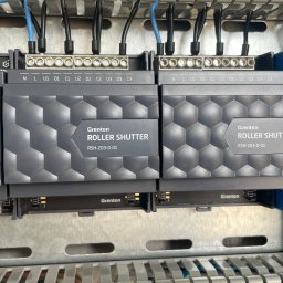 Qualitas Marek Zawadzki - Panel sterowania z zamontowanymi modułami Grenton BUS Module i Roller Shutter oraz zasilaczem TDK-Lambda, widoczne kable i złącza.