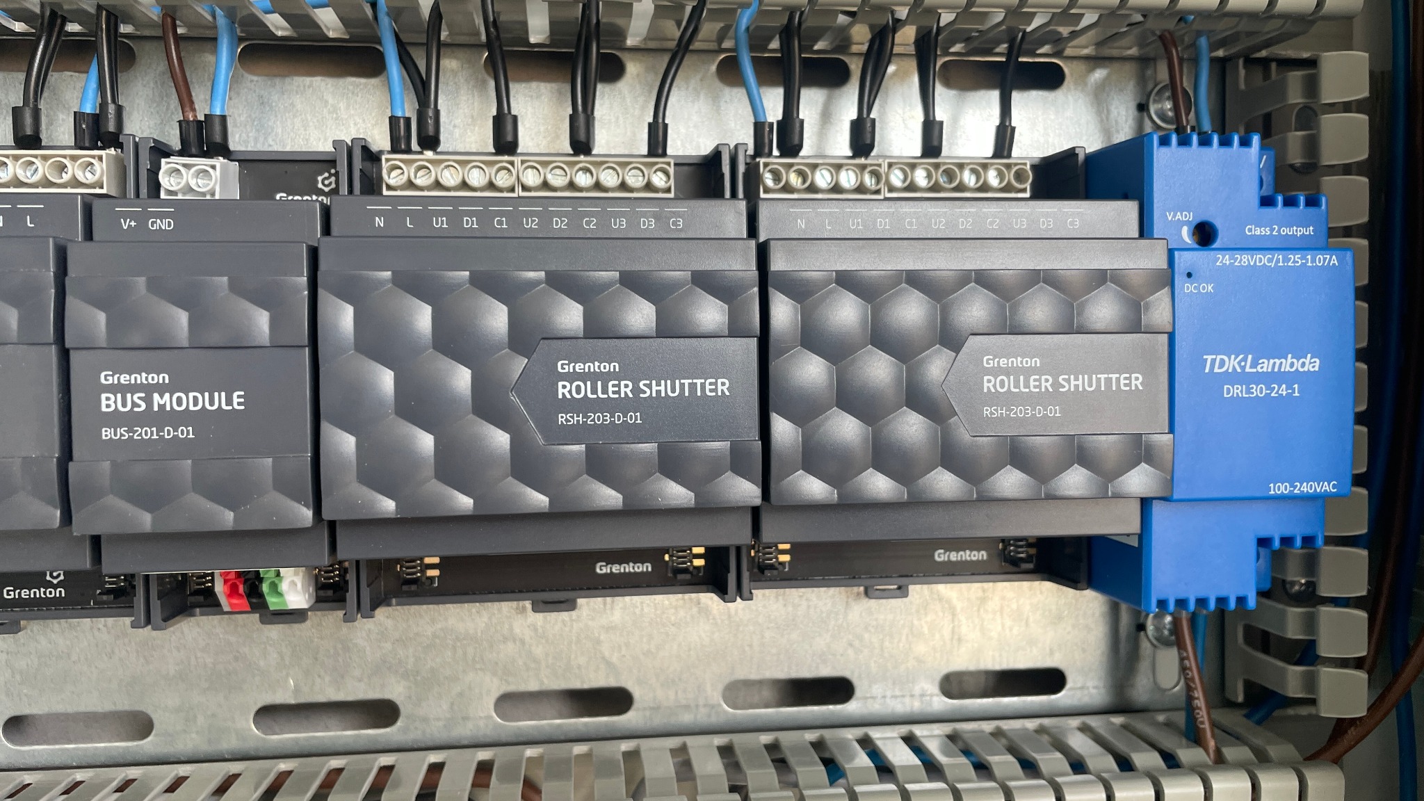 Panel sterowania z zamontowanymi modułami Grenton BUS Module i Roller Shutter oraz zasilaczem TDK-Lambda, widoczne kable i złącza.