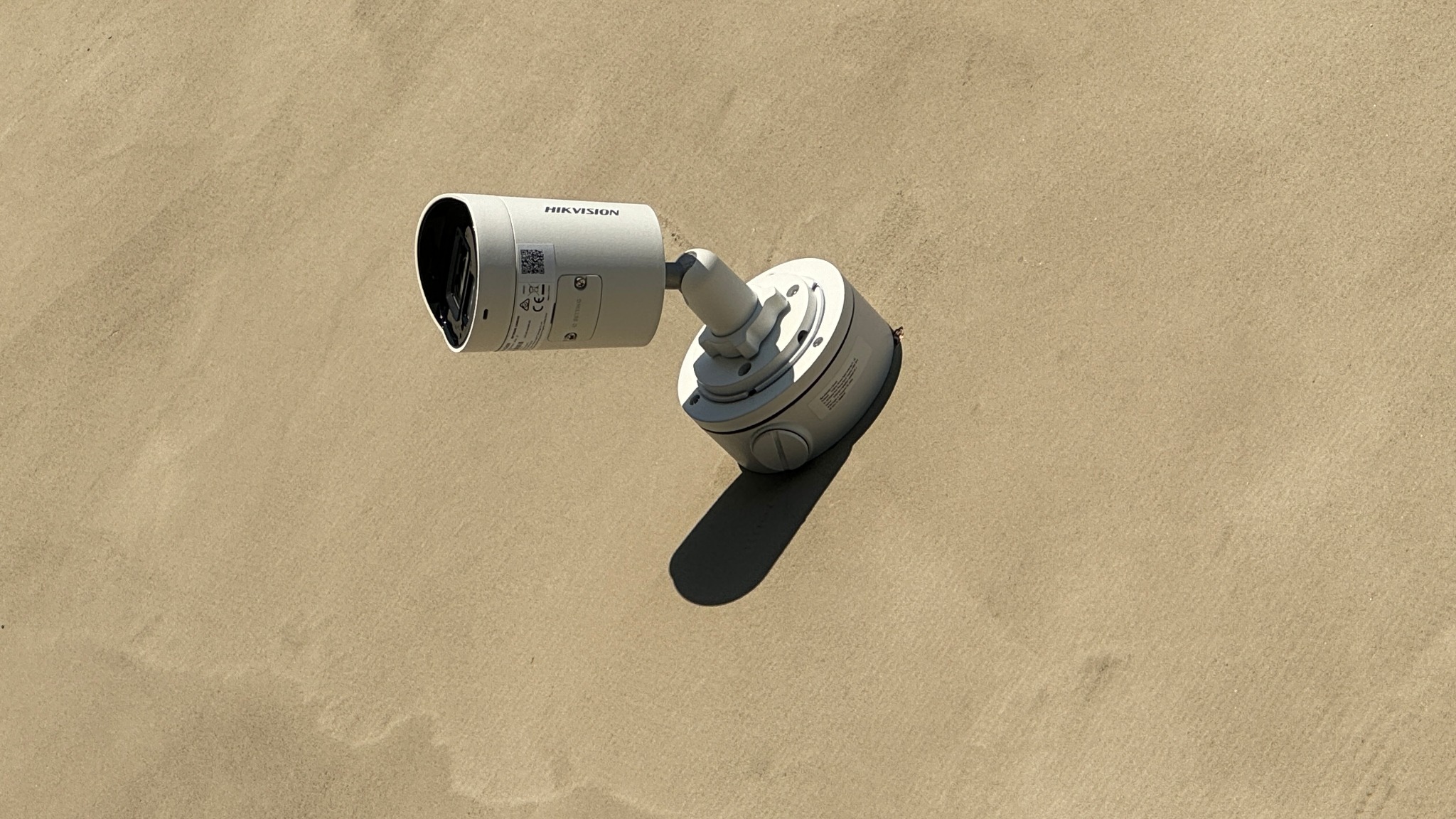 Kamera monitoringu marki Hikvision zamontowana na beżowej ścianie zewnętrznej, widoczne śruby mocujące i cień kamery.