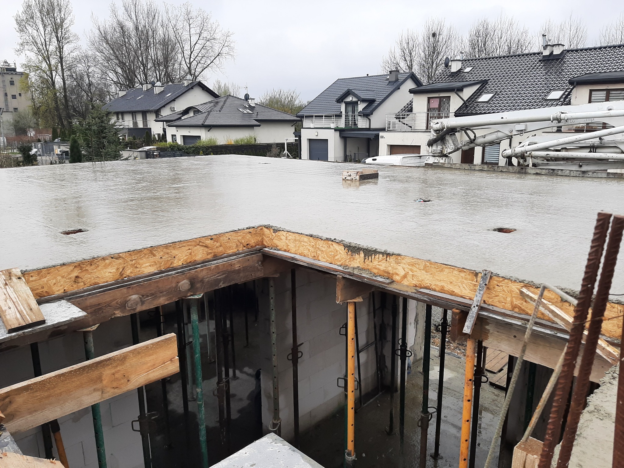 Wylewanie betonowego stropu na szalunkach z widocznymi podporami i zbrojeniem, w tle zabudowa jednorodzinna.