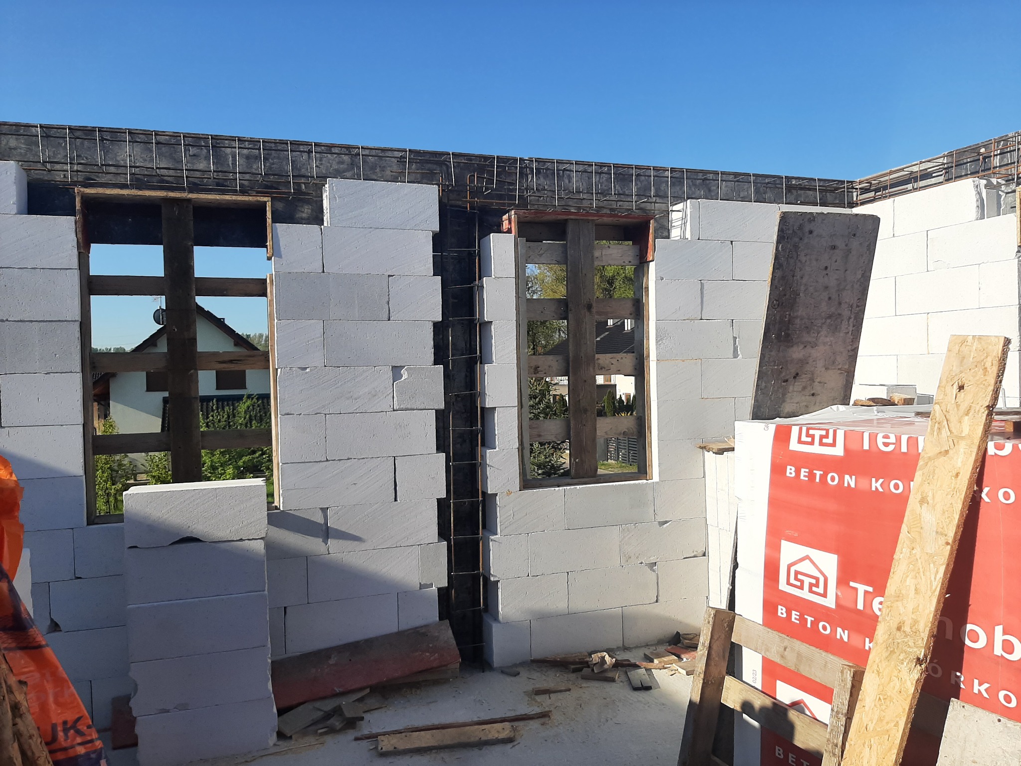 Wznoszenie ścian z betonu komórkowego Ytong, widoczne zbrojenie nadproży okiennych, paleta z bloczkami Termobet na pierwszym planie, budowa w trakcie.