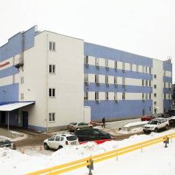 PRIMALINEPROJEKT Sp. z o. o. - Zewnętrzny widok na dwukolorowy budynek usługowy z płaskim dachem, z zaparkowanymi samochodami i zaśnieżonym otoczeniem w zimowy dzień.