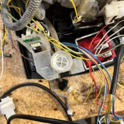 Wnętrze uszkodzonego ekspresu do kawy z widocznymi przewodami, elementami plastikowymi i śladami po kawie.