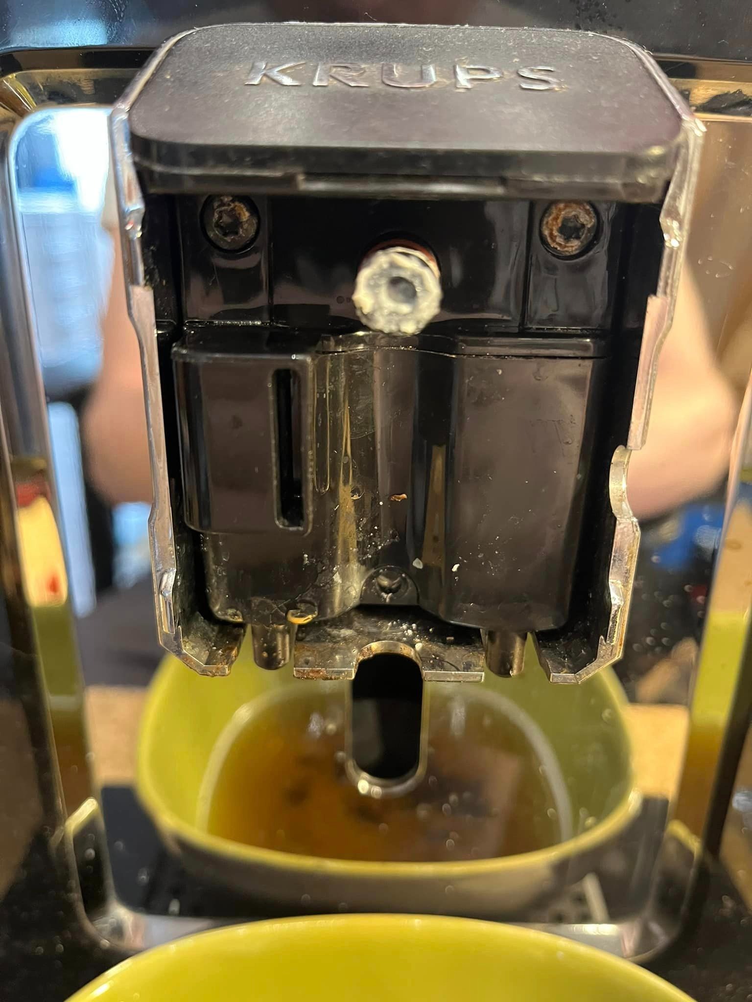 Wnętrze ekspresu Krups z widocznym pojemnikiem na wodę i resztkami kawy w żółtej miseczce, ślady użytkowania i kamienia na elementach.