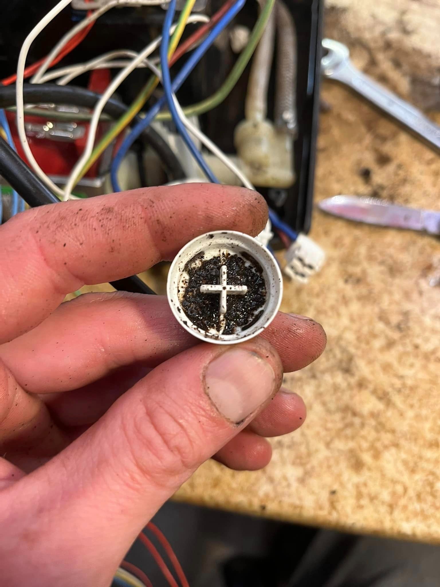 Zanieczyszczona część ekspresu do kawy trzymana w dłoni, widoczne przewody i narzędzia w tle.