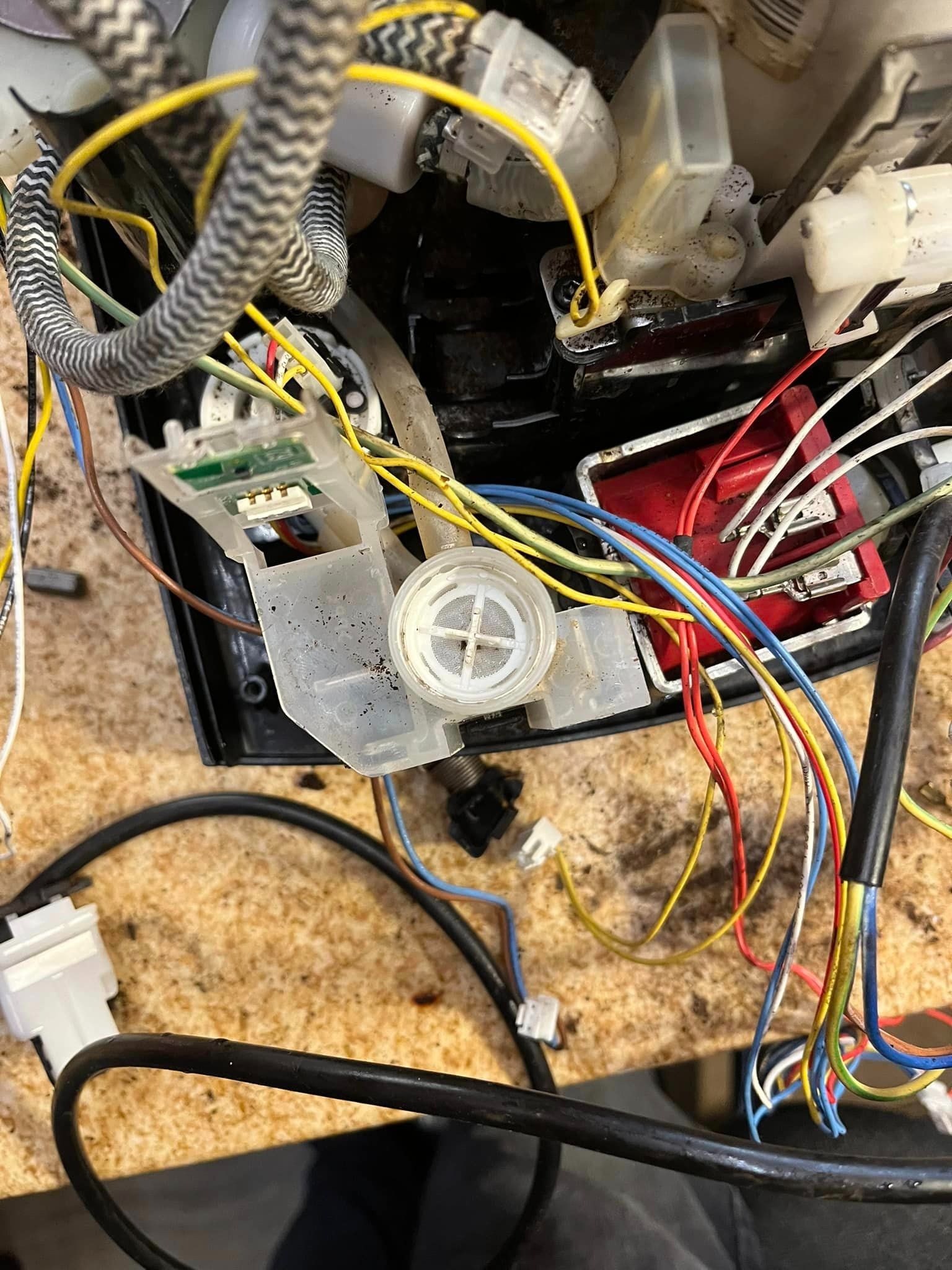 Wnętrze uszkodzonego ekspresu do kawy z widocznymi przewodami, elementami plastikowymi i śladami po kawie.