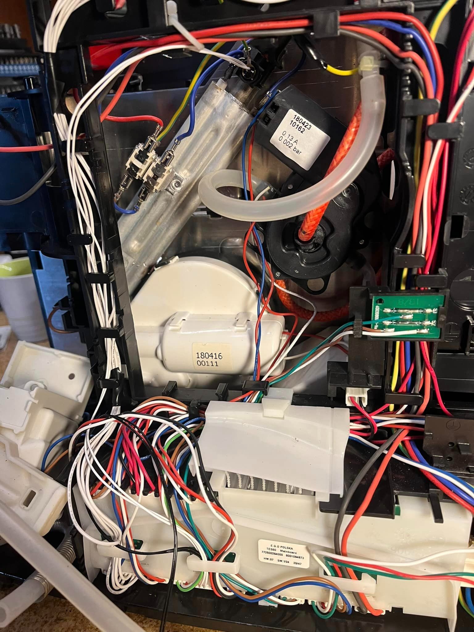 Wnętrze ekspresu do kawy z widocznymi elementami elektronicznymi, przewodami, rurkami i podzespołami, ukazujące stopień skomplikowania urządzenia.