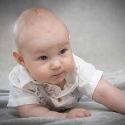 DUALART_PHOTOGRAPHY - Niemowlę w białej koszuli i szarych szelkach leżące na miękkim, szarym kocyku, zamyślone spogląda w bok.