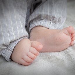 DUALART_PHOTOGRAPHY - Małe stópki niemowlęcia w pasiastych spodniach na miękkim, szarym kocyku.