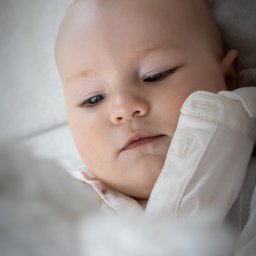 DUALART_PHOTOGRAPHY - Portret niemowlęcia w białej koszuli, leżącego na miękkim, białym tle, z delikatnym światłem podkreślającym rysy twarzy.