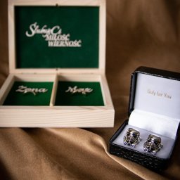 DUALART_PHOTOGRAPHY - Otwarta drewniana szkatułka na obrączki z napisem 'Ślubuję Ci Miłość Wierność' i przegródkami 'Żona' i 'Mąż' obok czarnego pudełka z mankietami do koszuli w kształcie hełmów Stormtrooperów...