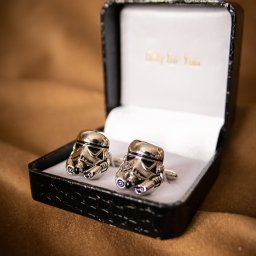 DUALART_PHOTOGRAPHY - Dwa srebrne spinki do mankietów w kształcie hełmów szturmowców z Gwiezdnych Wojen w czarnym pudełku prezentowym z napisem 'Only for You' na białym tle, leżące na brązowym materiale.