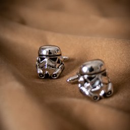 DUALART_PHOTOGRAPHY - Dwie srebrne spinki do mankietów w kształcie hełmów szturmowców z Gwiezdnych Wojen na beżowym, miękkim tle.