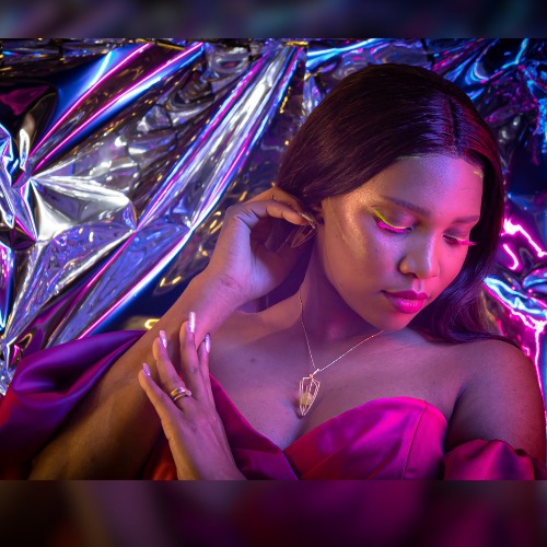 Portret kobiety z neonowym makijażem oczu i różową sukienką na tle srebrnej folii z neonowym oświetleniem.