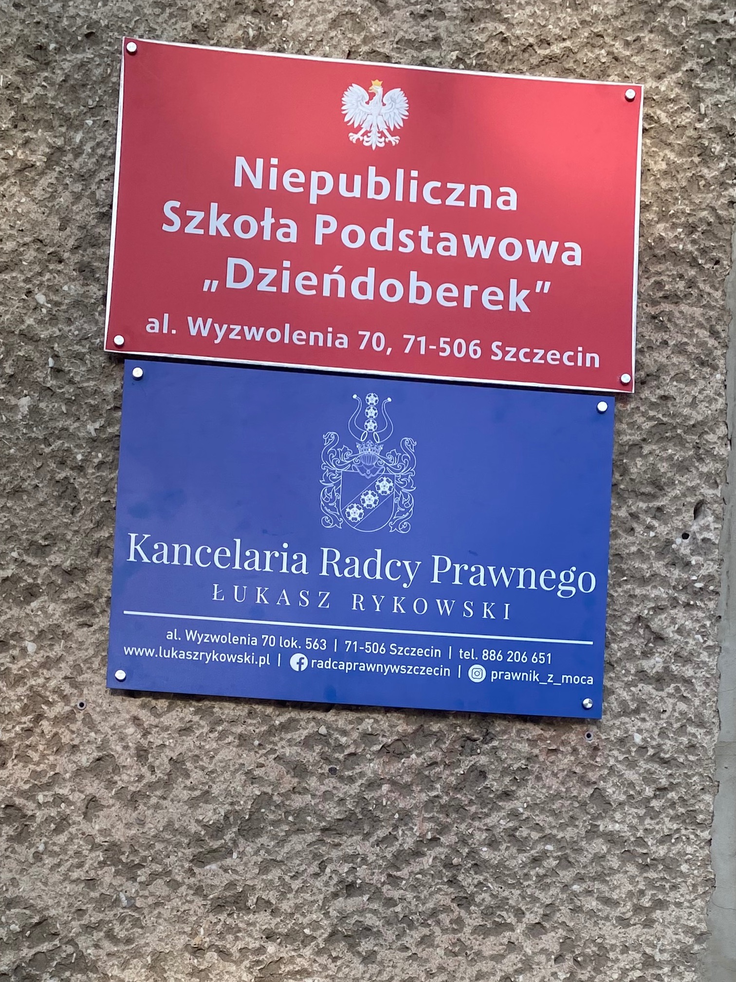 Tablica informacyjna: Kancelaria Radcy Prawnego Łukasz Rykowski w Szczecinie, adres al. Wyzwolenia 70. Nad tablicą szkoły podstawowej.
