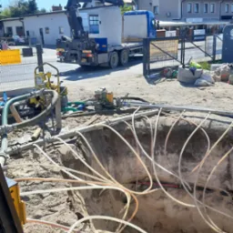 Wykop z licznymi rurami doprowadzonymi do wnętrza, maszyny budowlane i dźwig w tle, przygotowanie do instalacji podziemnej.