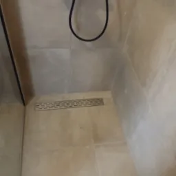 Beżowe płytki w kabinie prysznicowej z czarną armaturą i odpływem liniowym. Minimalistyczne wykończenie, nowoczesny design, jasne wnętrze.