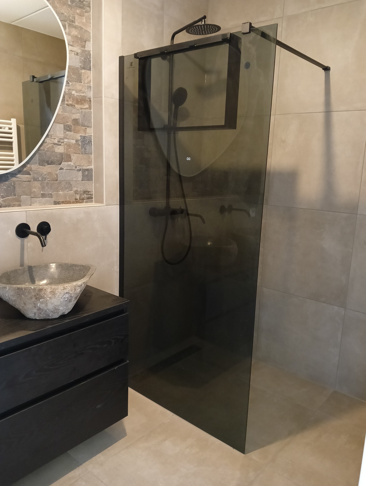 Nowoczesna łazienka z kabiną prysznicową typu walk-in, umywalką z kamienia i lustrem. Stonowana kolorystyka, minimalistyczny design.