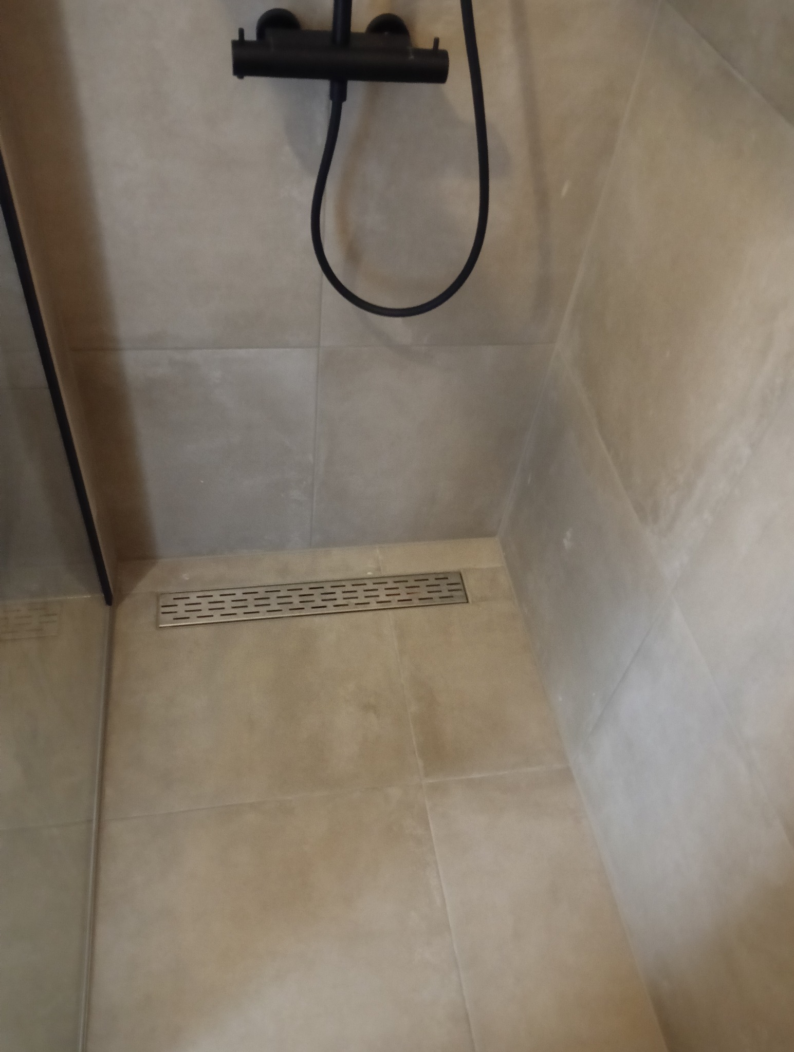 Beżowe płytki w kabinie prysznicowej z czarną armaturą i odpływem liniowym. Minimalistyczne wykończenie, nowoczesny design, jasne wnętrze.