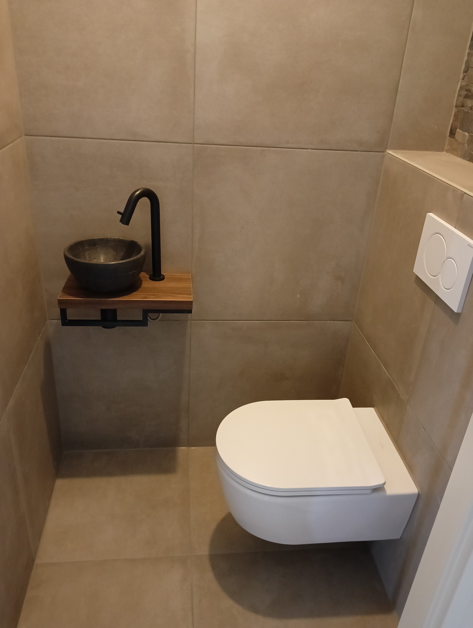 Nowoczesna łazienka w Toruniu z podwieszaną toaletą i umywalką z czarną armaturą na drewnianym blacie, wykończona płytkami w odcieniach beżu i szarości.