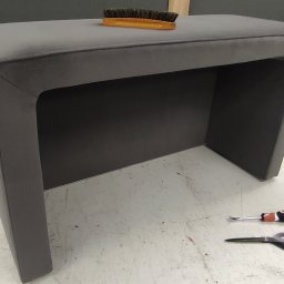 Hako Meble - Szary, tapicerowany stołek z zaokrąglonymi krawędziami, szczotka do czyszczenia tapicerki na górze, obok leżą nożyczki i śrubokręt do tapicerowania.