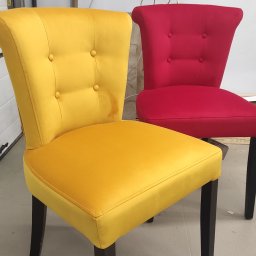 Hako Meble - Dwa krzesła tapicerowane: jedno żółte z plamą na oparciu, drugie czerwone, oba z czarnymi nogami i guzikami na oparciu, na tle białej ściany.