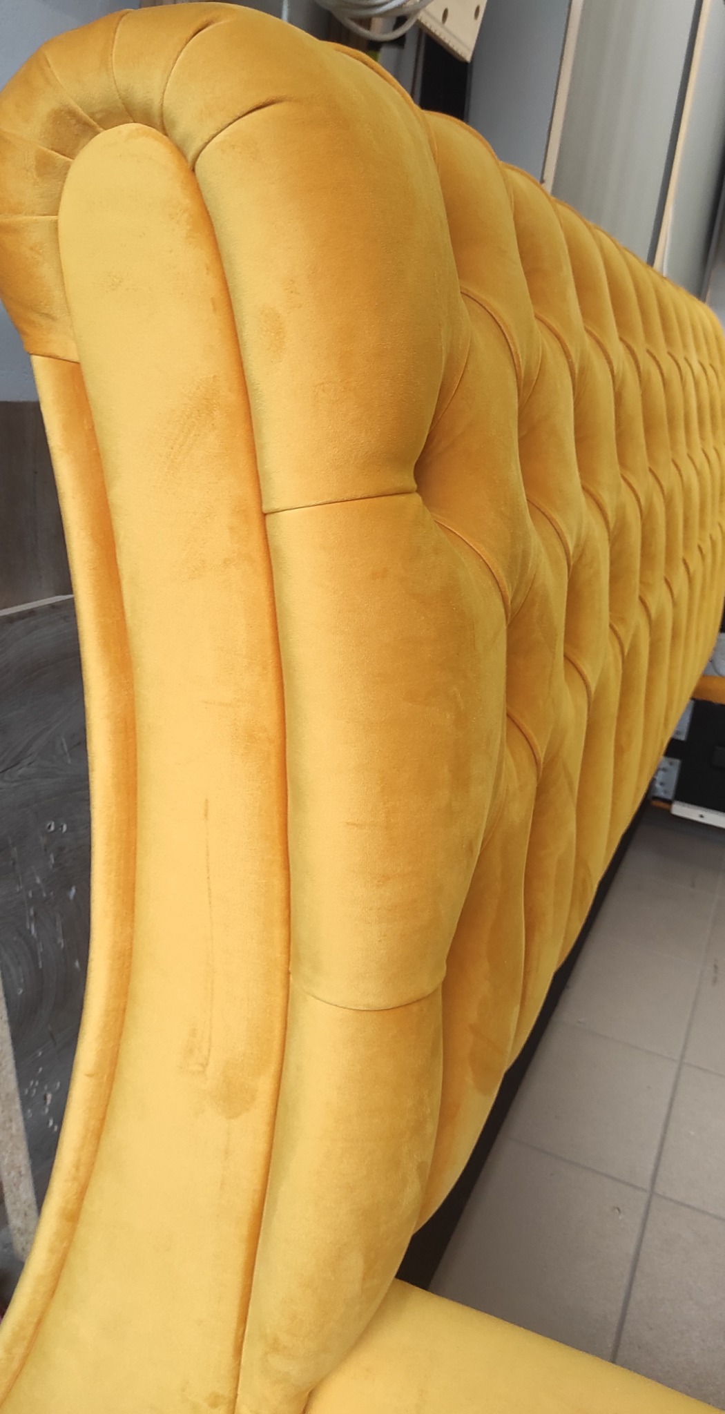 Fragment oparcia sofy z żółtego weluru z głębokimi pikowaniami, widoczne drobne zabrudzenia na materiale.