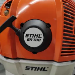 Pomarańczowo-biała dmuchawa spalinowa Stihl BR 700 z widocznym logo i uchwytem rozrusznika, ukazana z bliska.