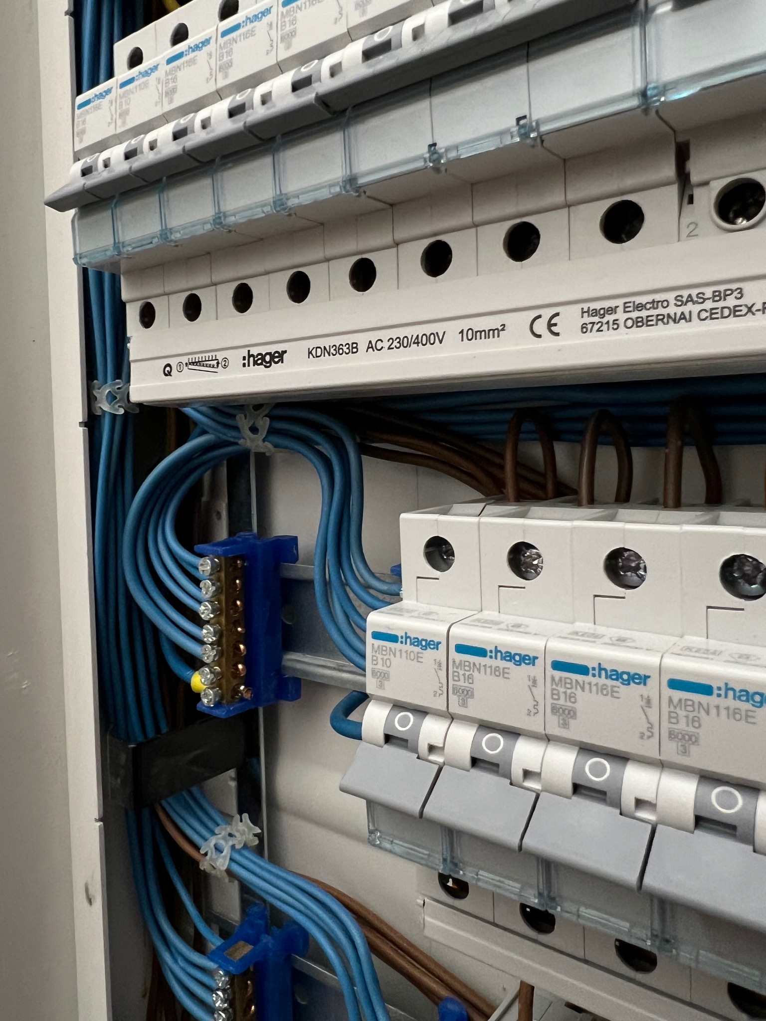 Nowa rozdzielnica Hager z niebieskimi przewodami i listwą zaciskową, zamontowana w szafce. Widoczne zabezpieczenia B10 i B16. Instalacja po modernizacji.