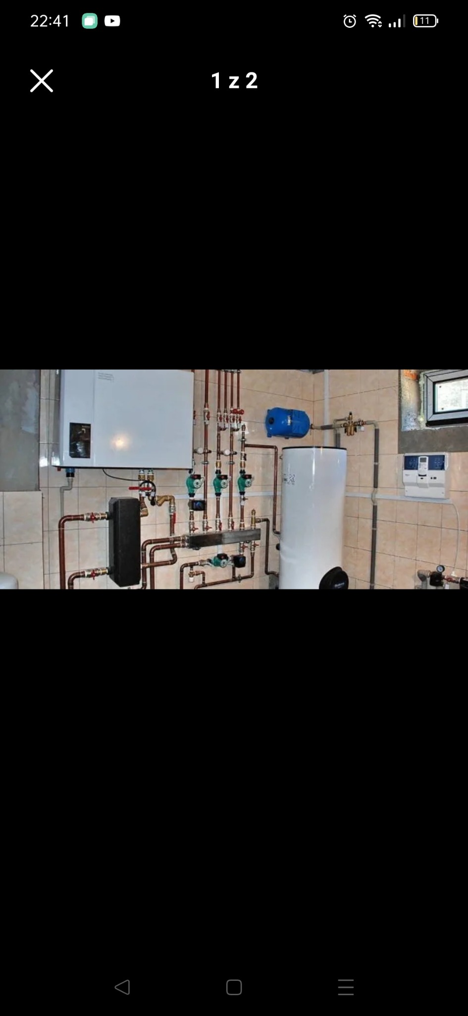 Złożona instalacja hydrauliczna z kotłem, zasobnikiem ciepłej wody, pompami obiegowymi i rozdzielaczem, zamontowana na ścianie wyłożonej kafelkami.