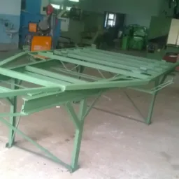 Zielona, metalowa konstrukcja ramy stołu spawalniczego na tle warsztatu z maszynami do obróbki metalu.