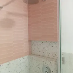 Wnętrze kabiny prysznicowej z różowymi, podłużnymi płytkami ułożonymi w cegiełkę oraz ścianą wykończoną lastryko, widoczny panel sterowania prysznicem i deszczownica