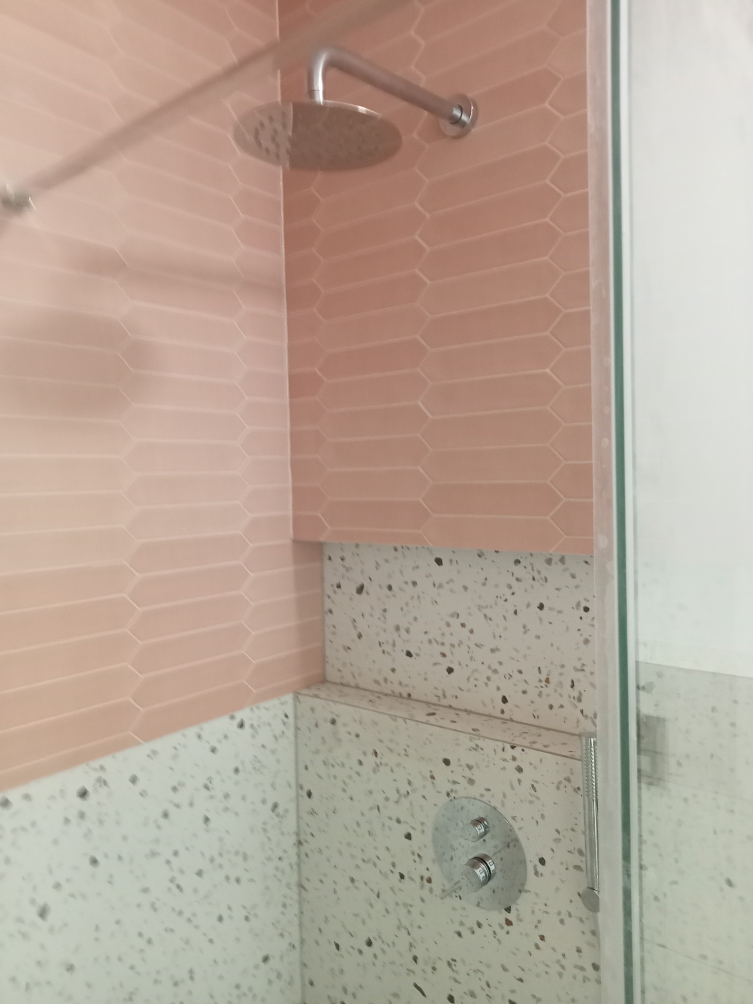 Wnętrze kabiny prysznicowej z różowymi, podłużnymi płytkami ułożonymi w cegiełkę oraz ścianą wykończoną lastryko, widoczny panel sterowania prysznicem i deszczownica