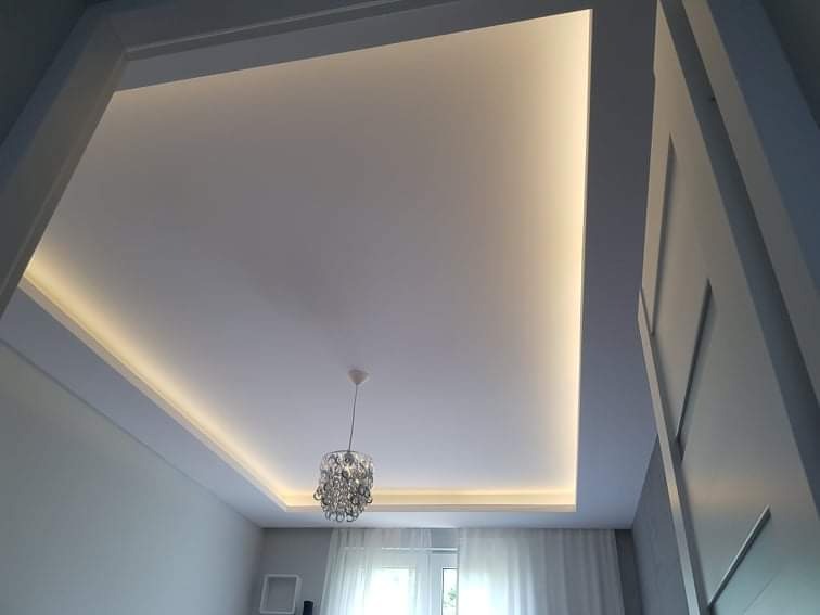 Nowoczesny sufit podwieszany z oświetleniem LED wzdłuż krawędzi i ozdobnym żyrandolem w centrum, widok z dołu.