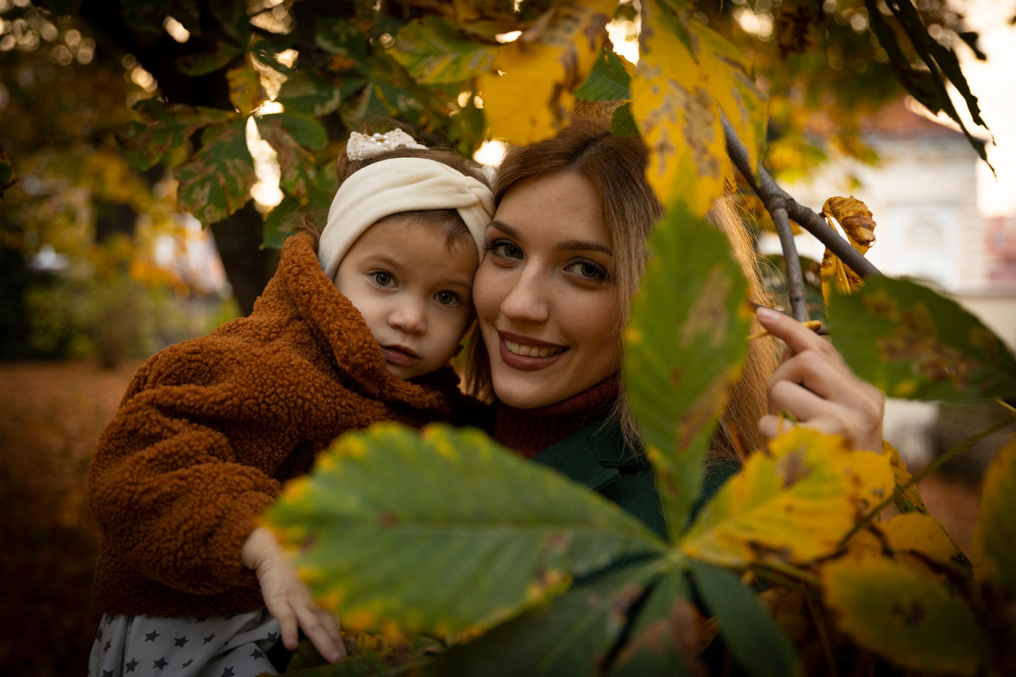 Portret matki z córką w jesiennej scenerii, liście kasztanowca w pierwszym planie, ciepłe oświetlenie.