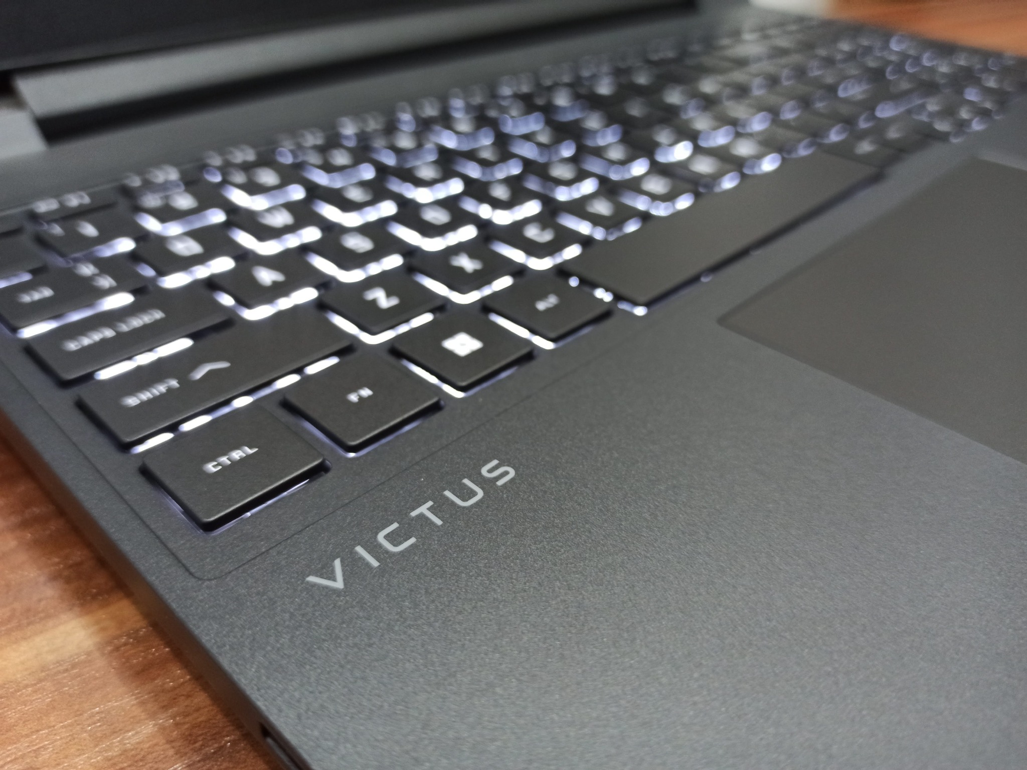 Ciemnoszary laptop HP Victus z podświetlaną klawiaturą, widok z góry na klawiaturę i touchpad.