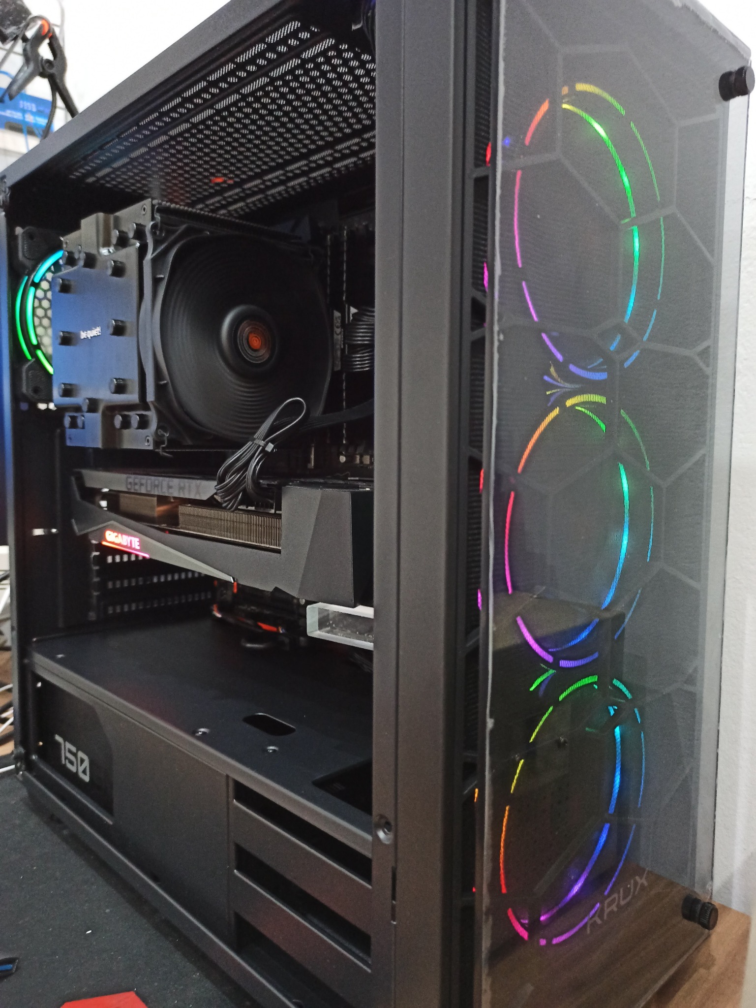 Wnętrze obudowy komputera stacjonarnego z widoczną kartą graficzną GeForce RTX, chłodzeniem procesora Be Quiet! i podświetlanymi wentylatorami RGB marki Krux na przednim panelu z siatki mesh.