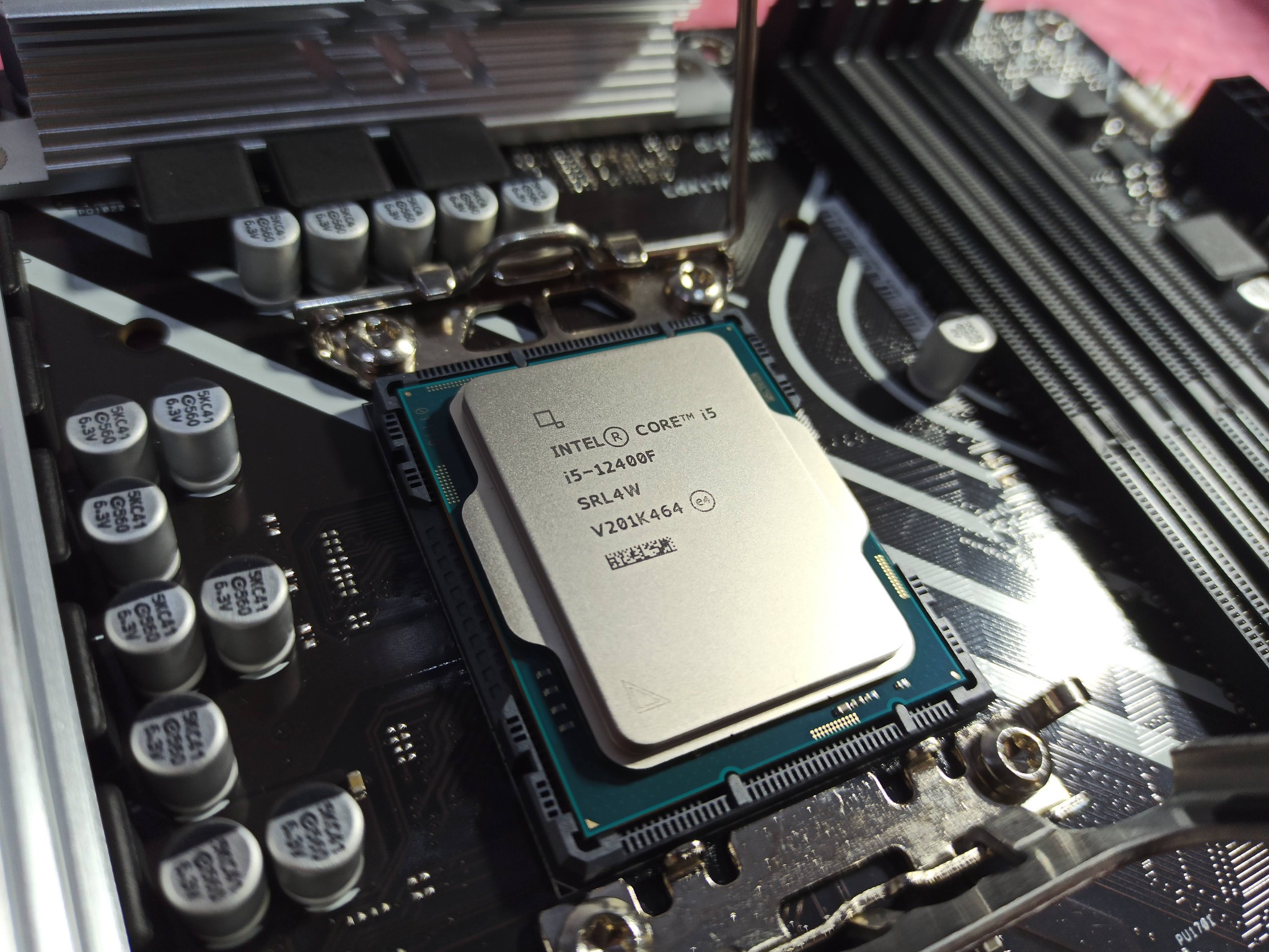 Procesor Intel Core i5-12400F umieszczony w gnieździe płyty głównej, widoczne kondensatory i sloty pamięci RAM.