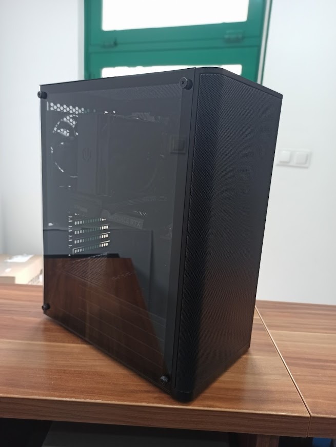 Czarna obudowa komputera stacjonarnego z widocznymi komponentami wewnętrznymi, w tym kartą graficzną RTX, umieszczona na drewnianym biurku w jasnym pomieszczeniu.