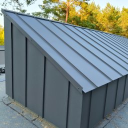 Ivan Marchenko VANBUD - Nowoczesne, grafitowe krycie dachu z blachy na budynku z widocznym tłem drzew. Estetyczne wykończenie detali i precyzyjne łączenia blacharskie.