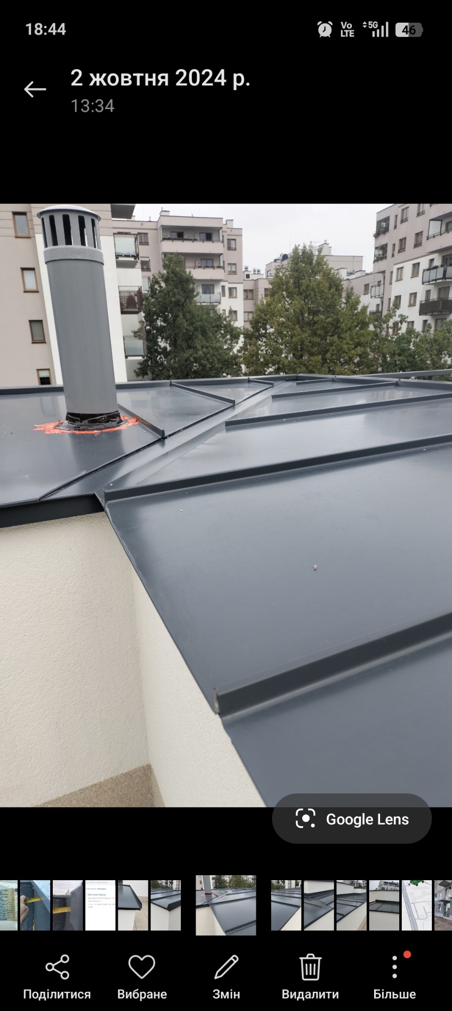 Szary dach z blachy na tle miejskiego krajobrazu. Widoczny komin wentylacyjny z pomarańczowym uszczelnieniem. Nowoczesne budownictwo, precyzyjne łączenia blach.