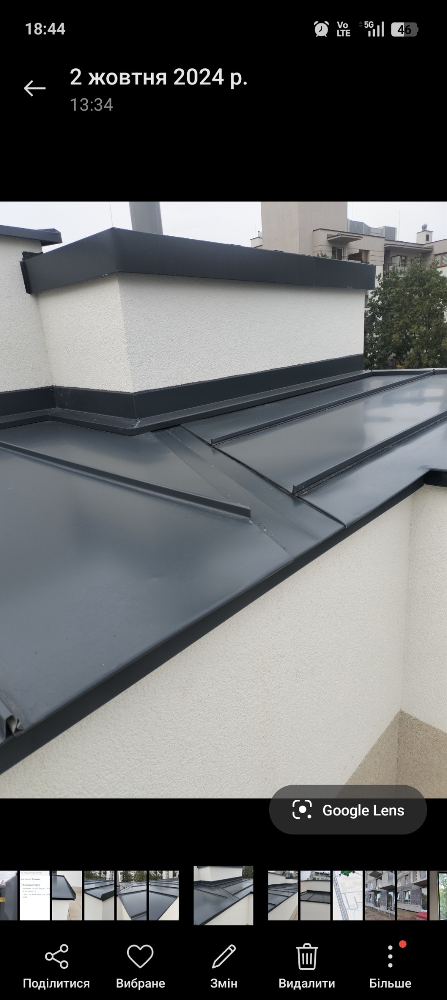 Szary dach z blachy na budynku z jasną elewacją. Widoczne obróbki blacharskie i fragment budynku w tle. Ujęcie z dołu, podkreślające detale wykonania.