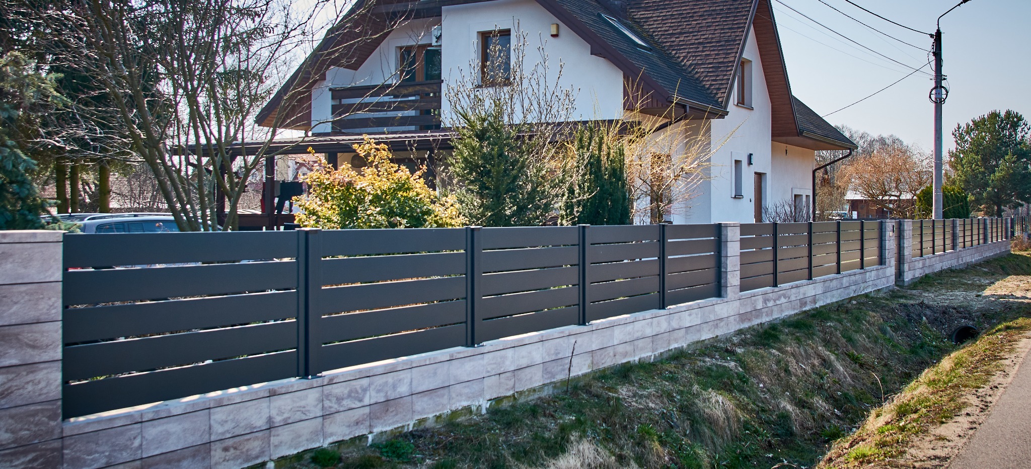 Nowoczesne, poziome ogrodzenie z szarych paneli na podmurówce z płytek w Gwizdałach, widok z zewnątrz posesji, dom w tle.