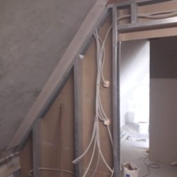 Arkadiusz Dublinowski - Szkielet ścianki działowej z profili metalowych w trakcie montażu, widoczne przewody elektryczne w peszlach i częściowo położona płyta gipsowo-kartonowa na poddaszu.